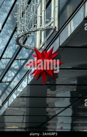 Christmas ornament in the form of a multi ended red star and electric lights hanging above the entrance to the building. Stock Photo