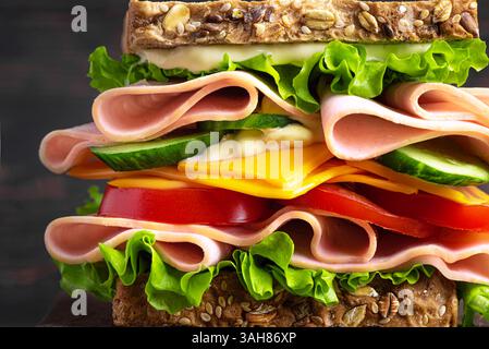 Big layered sandwich with ham, lettuce, cheddar cheese, tomato and cucumber on rustic wooden background,  close up detailed. Healthy lunch sandwich wi Stock Photo