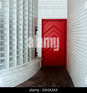 Striking Art Moderne-style red door framed by curved glass block and white brick walls, creating a bold and streamlined entryway in Chicago Stock Photo