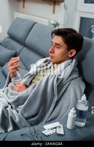Man feeling cold and lying in the bed and blowing his nose with nasal spray. Man is using nasal spray and take medical pills and medicaments for illne Stock Photo