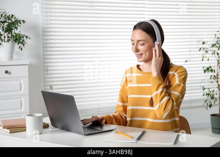 Smiling woman learning online using laptop at table indoors. Self-study Stock Photo