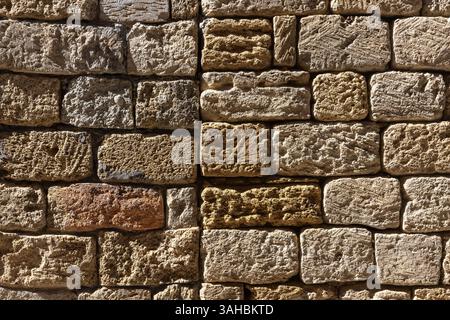 Natural shell rock stone brick wall showcasing its rustic rough texture and earthly tones under strong sunlight. Suitable background for architectural Stock Photo