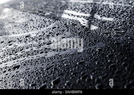 A detailed shot of water droplets forming on a smooth metallic surface of a car, reflecting light and presenting a textured, shimmering appearance, em Stock Photo