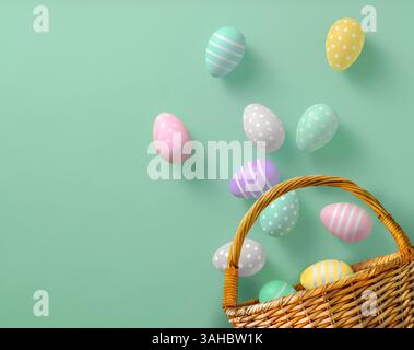 Bright Easter eggs in pastel colors scattered from a charming basket on a pale green background Stock Photo