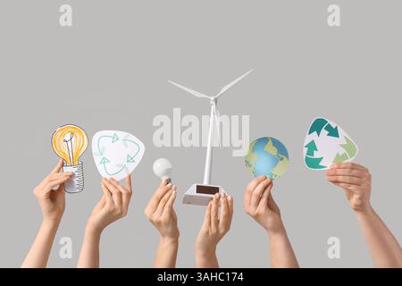 Female hands with wind turbine model, light bulbs and recycle signs on light background. Ecology concept Stock Photo
