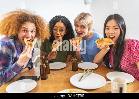 Group of young diverse friends eating pizza slices and drinking beer, having fun together at home Stock Photo