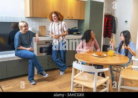 Happy multi ethnic friends spending leisure time together, having breakfast and talking in a modern kitchen Stock Photo