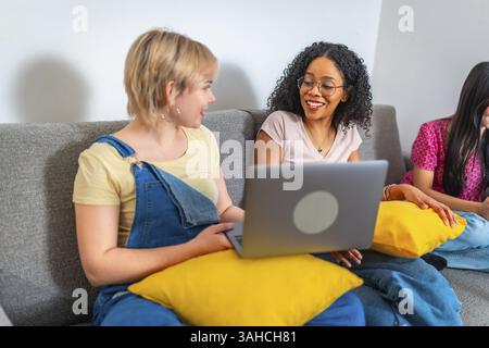 University students working together on a project using laptop, discussing and sharing ideas while sitting on a comfortable sofa Stock Photo