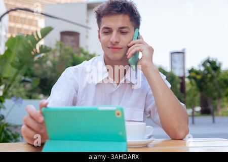 Caucasian businessman using tablet and phone at outdoor cafe on a sunny day Stock Photo