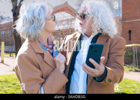 Senior couple using smartphone outdoors, enjoying technology and digital trends. Stock Photo