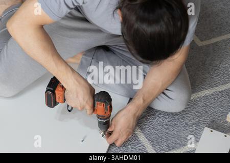 Man assembling wardrobe at home using power drill. Stock Photo