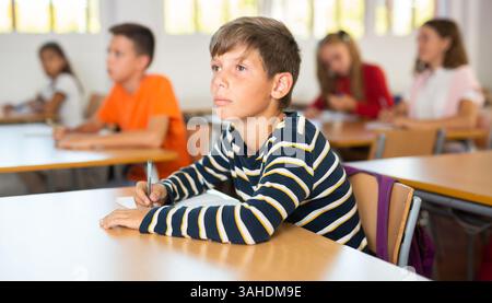 Focused preteen schoolboy writing in workbook during lesson Stock Photo