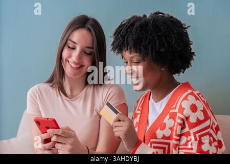 Two happy women sitting on couch smiling while looking at smartphone screen Stock Photo