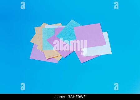 A stack of multicolored square paper sheets arranged on a vibrant blue surface, ideal for crafts, notes, or design projects. Stock Photo