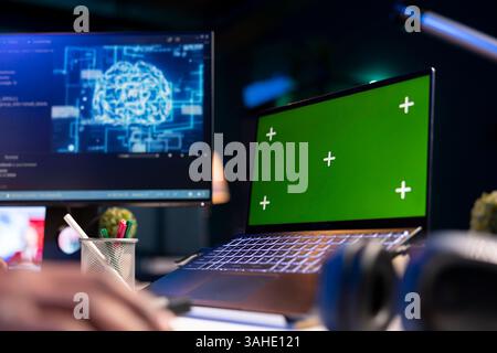 Black person programming neural network code with a green screen on computer to build databases. System engineer working from home while looking at data center security servers. Stock Photo