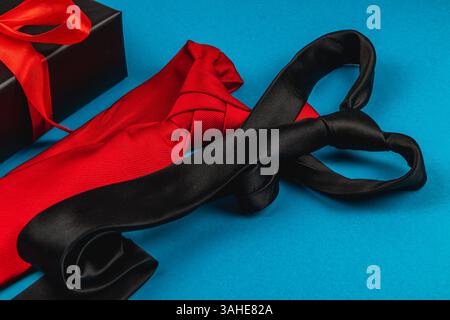 Two elegant ties rest on a vibrant blue background, complementing a black gift box adorned with a red ribbon, perfect for father's day celebrations an Stock Photo