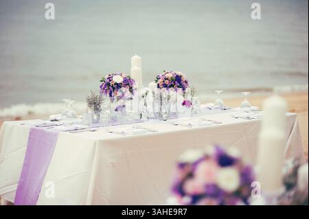 romantic wedding reception party's dinner table with a bouquets on the beach and blue sea in background in the afternoon Stock Photo
