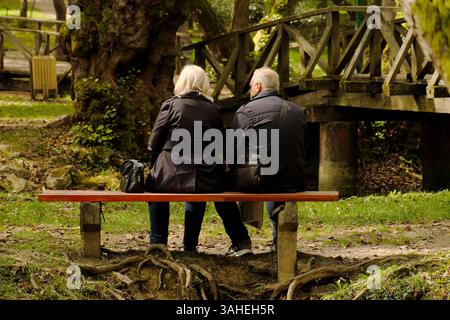 rear view couple sitting on bench in the park of the Bosna River, Sarajevo, Bosnia and Herzegovina Stock Photo