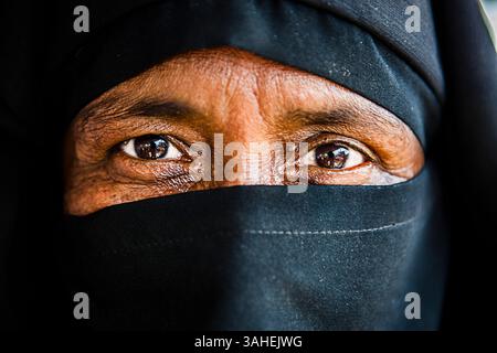 Close-up of elderly woman’s expressive eyes wearing a black niqab, symbolizing tradition, mystery, and strength in cultural identity. Stock Photo