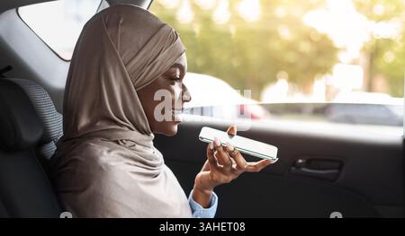Black Muslim Woman Sending Voice Message And Using Laptop In Car Stock Photo
