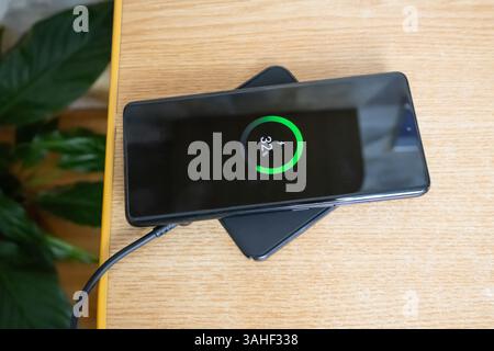 Smartphone placed on a wireless charging pad while charging on a wooden surface, top view Stock Photo