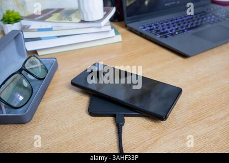 Smartphone placed on wireless charging pad on working table, top view Stock Photo