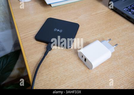 White charger used to charge empty battery next to black wireless charging pad on the table, top view Stock Photo
