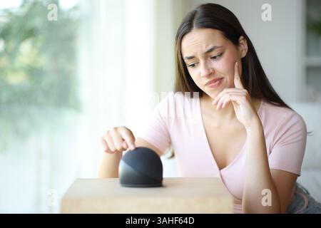 Disappointed woman using smart speaker sitting on a couch at home Stock Photo