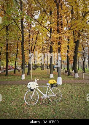A white bicycle decorated with flowers placed against colorful trees in the autumn park Stock Photo