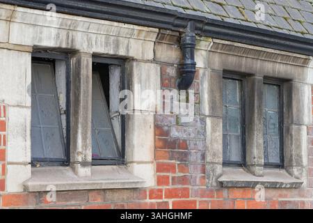 Old metal framed windows with stone and brick surrounds. Iron gutting and slate roof tiles. Architectural details found on streets of central London. Stock Photo