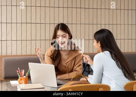 Learning and Digital Tools. Two friends review digital materials on a laptop during their study time. Stock Photo