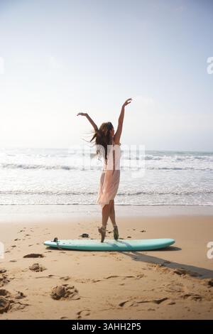 Cinematic shot of ballerina in pink dress balancing en pointe on beach surfboard Stock Photo