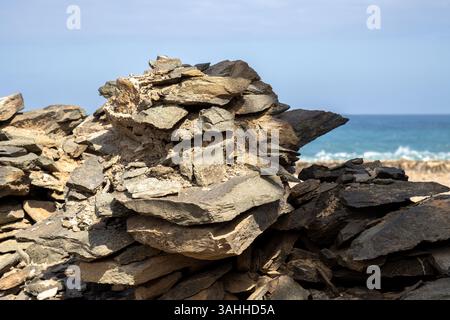 Enligted (by sunlight)fence made of thin pieces of a stone without concrete. Atlantic ocean and blue sky with clouds in a blurry background. Las Palma Stock Photo