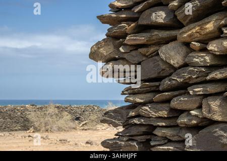 Enligted (by sunlight)fence made of thin pieces of a stone without concrete. Atlantic ocean and blue sky with clouds in a blurry background. Las Palma Stock Photo