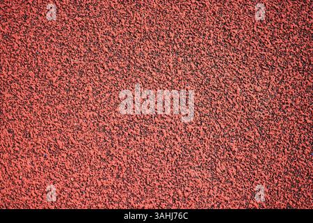 Red sports field rubber coating close up macro view. Playground paving background texture extremely close. Stock Photo