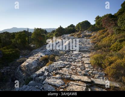 Ancient stone pathway winding through a rocky landscape under a clear blue sky. Stock Photo
