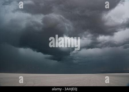 Dark storm clouds loom over a vast, flat desert landscape, creating a dramatic sky. Bonneville Salt Flats, Utah, USA Stock Photo