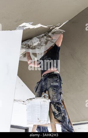 Male builder at work overalls plastering and restoring old wall using a construction trowel. Stock Photo