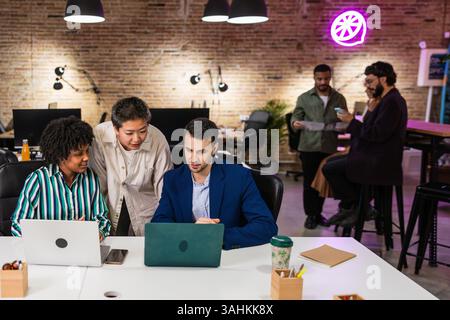 Multi ethnic team collaborating on laptops in modern office Stock Photo
