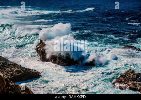 Waves crashing against rocky coastline under a clear blue sky. Monterey, CA, USA Stock Photo