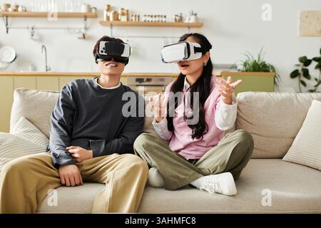 A joyful young couple engages in an immersive virtual reality experience on their couch. Stock Photo