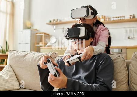 A young couple enjoys virtual reality gaming together, immersed in their cozy living room. Stock Photo