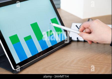 A skilled professional analyzes data trends on a tablet with a stylus for effective insights into metrics Stock Photo