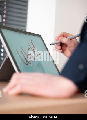 A person is using a sleek digital tablet to creatively write the word Work with a stylus in hand Stock Photo