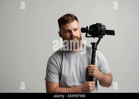 Bearded videographer holding camera which set on 3-axis gimbal. Videographer using steadicam. Stock Photo