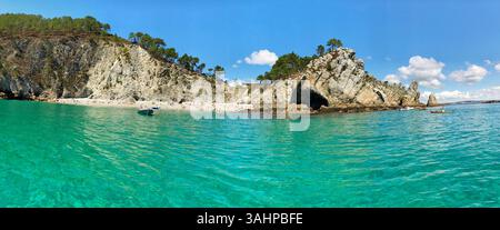 Explore a pristine coastal scene featuring turquoise waters, rugged cliffs, trees, and clear blue skies. Vivid and scenic panorama ideal for beach vac Stock Photo
