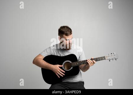Bearded guitarist man with a black guitar playing a song in a studio white background. Stock Photo