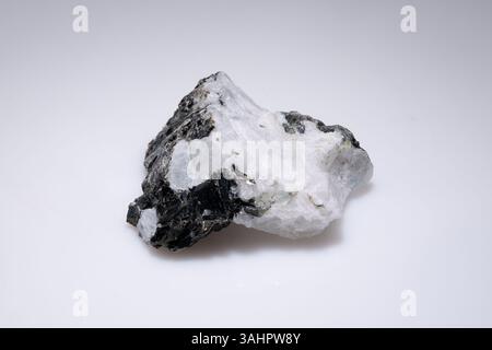 Raw moonstone specimen with black inclusions against a plain white background, showcasing its natural texture and iridescent sheen. Stock Photo