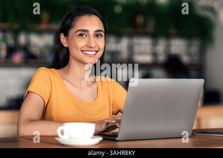 Cheerful female student using laptop at cafe Stock Photo