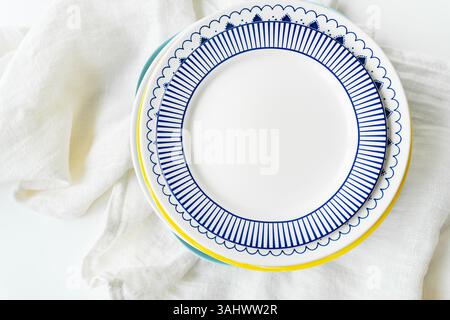 Stylish blue and white patterned plates stacked on a white linen tablecloth, creating a clean and modern table setting. Stock Photo